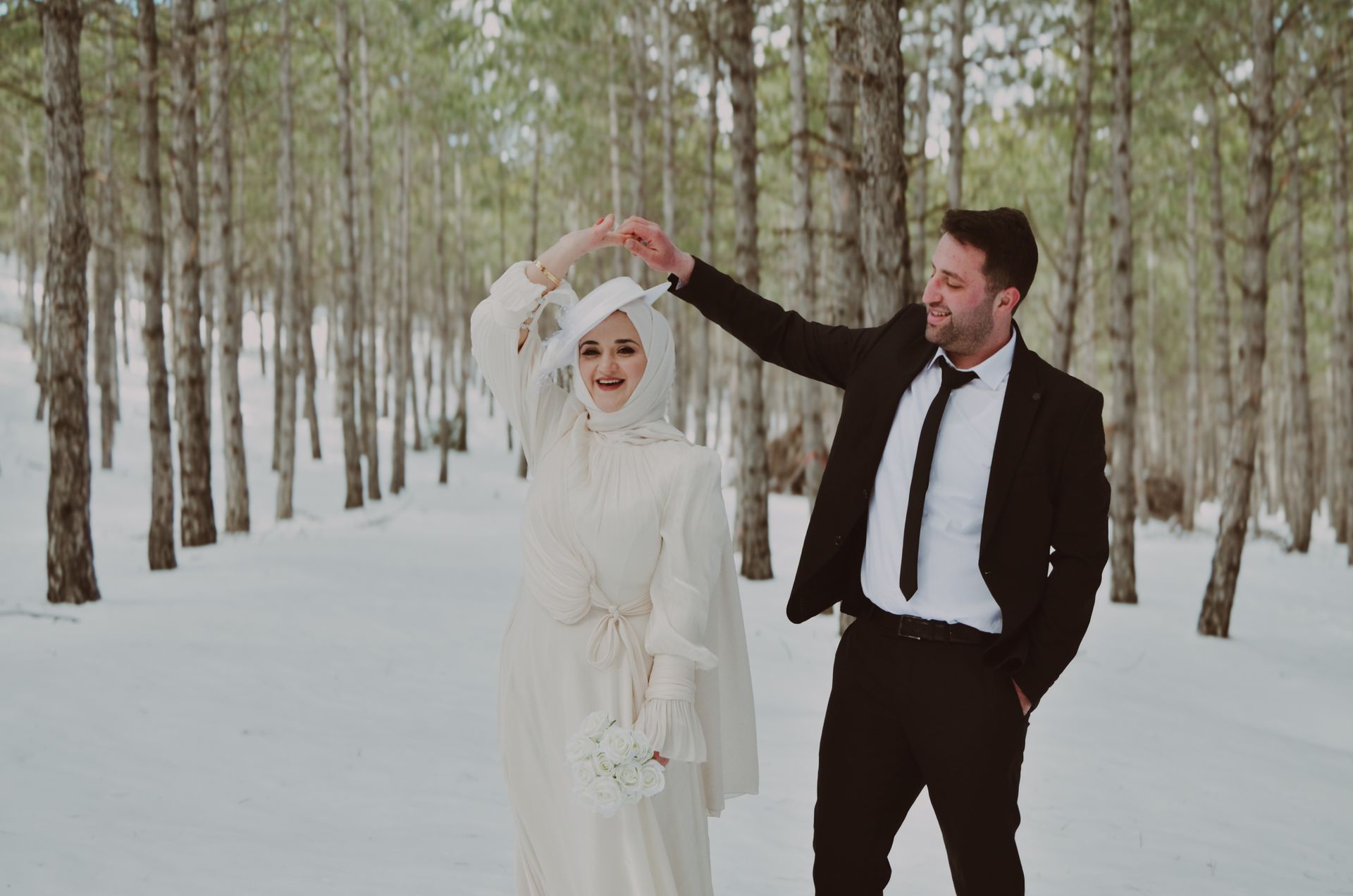Bride and groom dancing in a snowy evergreen forest on their winter wedding day
